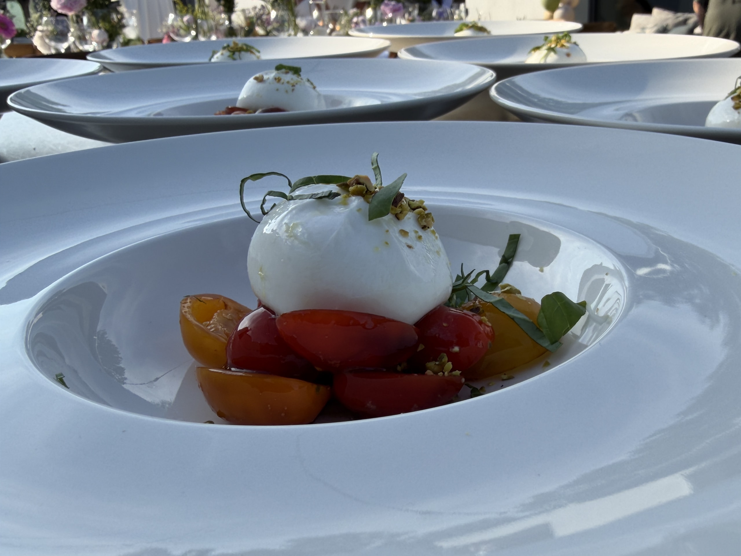 Voorgerecht van burrata met kleurige tomaatjes op een diep wit bord.