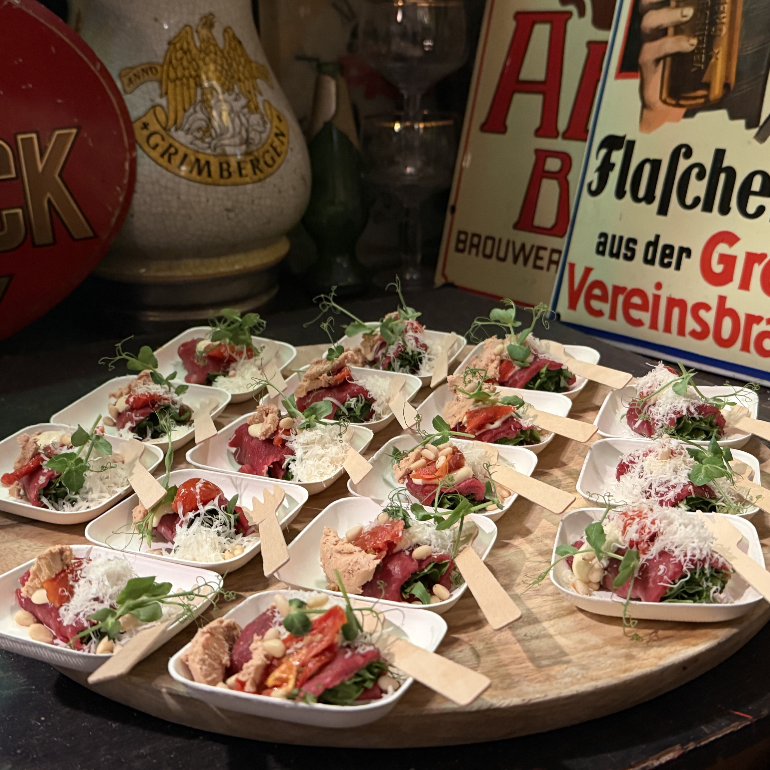 Houten plateau vol bakjes carpaccio met kaas en kiemgroente, tussen oude reclameborden.