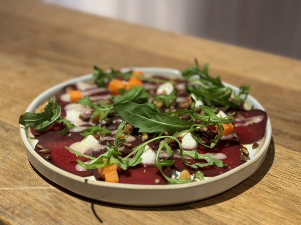 Carpaccio met rucola, zachte kaas, blokjes wortel en noten op een bord op een houten tafel.