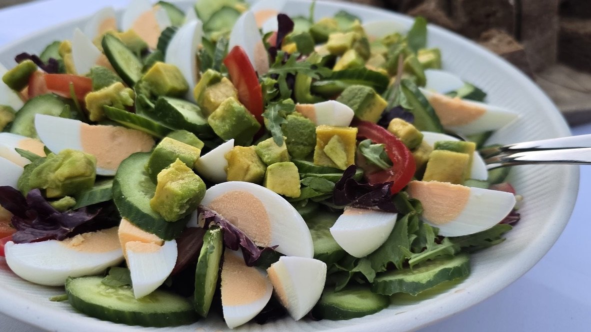Schaal met groene salade, gekookt ei, avocado, komkommer en tomaat.
