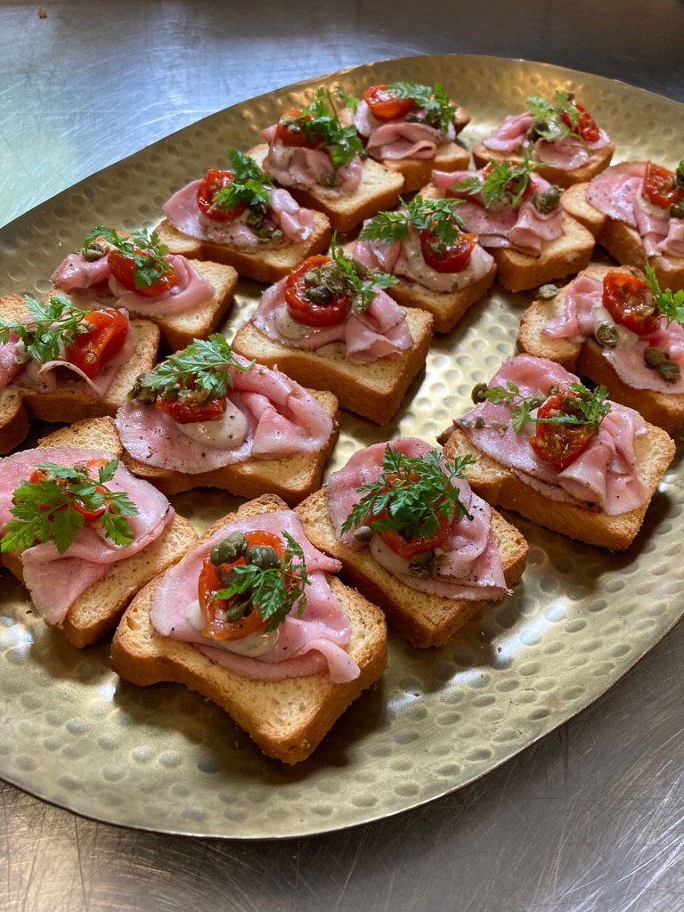 Schaal met toastjes met ham, tomaat, kappertjes en peterselie.